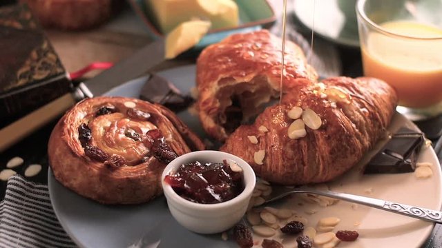 Pouring honey on pastries. French breakfast with pastries, orange juice and coffee