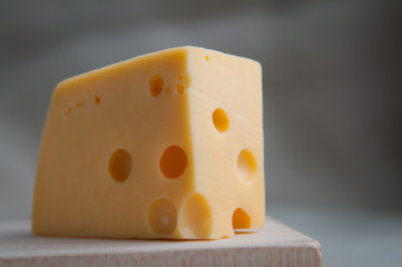 A piece of maasdam cheese with holes served in rustic style on a wooden board. Close up. Eco food, meal, lunch concept