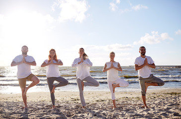 group of people making yoga in tree pose on beach