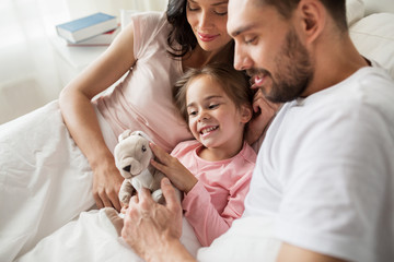 happy child with toy and parents in bed at home