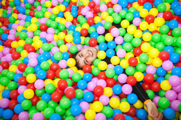 Happy and funny young man relaxing in many colorful balls 
