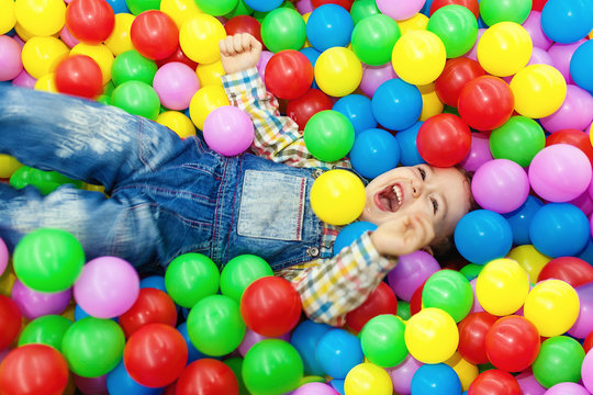 Happy little boy laughing in colorfl balls.
