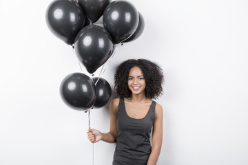 Brunette woman smiling and holding a bunch of black balloons, indoors