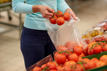 woman with bag buying tomatoes at grocery store