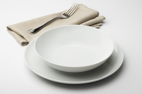 Empty round white plate and bowl with napkin and fork