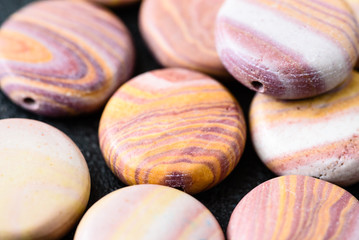 Collection of multicolored coin shaped hickoryite beads on black cast iron plate. Hickoryite is a banded variety of rhyolite.
