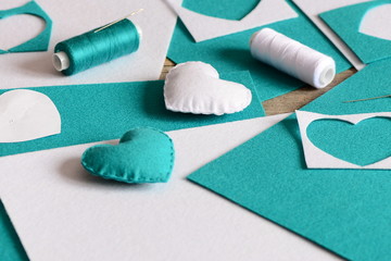 Small stuffed hearts decor. Hearts made of felt, thread, felt sheets and scraps, needle on table....