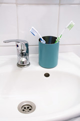 Two green and blue toothbrushes in the metal glass on the white sink