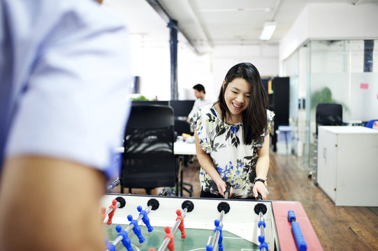 Asian and mixed race co-workers playing table football in office