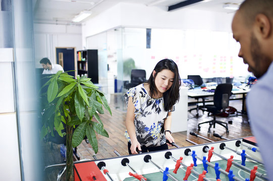 Asian and mixed race co-workers playing table football in office