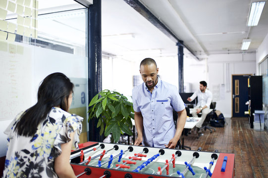 Asian and mixed race co-workers playing table football in office