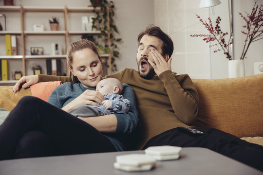 Tired father and mother sitting with baby on couch