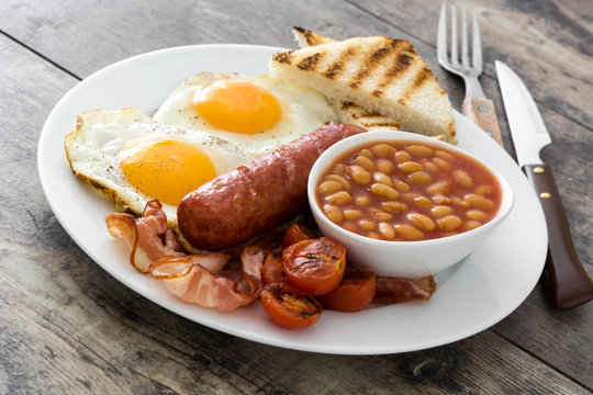 Traditional full English breakfast with fried eggs, sausages, beans, mushrooms, grilled tomatoes and bacon on wooden background