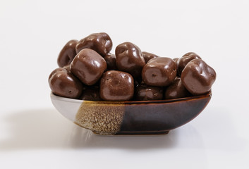 Chocolate dragees in a small dish on a white background.