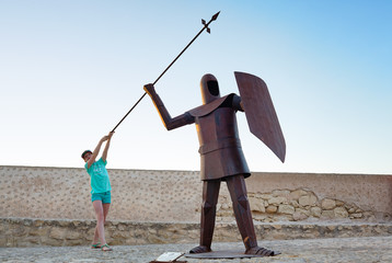 Girl and warrior. Santa Barbara castle metal with spear shield. Alicante, Spain. - obrazy, fototapety, plakaty
