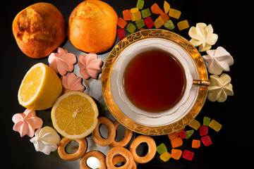 Cup of tea with a lemon and sweets. Still life against a dark background