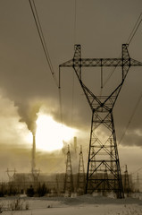 Gas power plant in cold winter landscape during sunset. Pipes with smoke. Power transmission tower foreground. Energy industry concept. Toned.