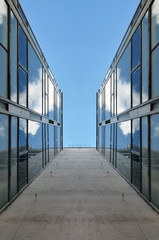 Looking up at the facade of a modern building with glass mirror walls against the blue sky. Symmetrical vertical view.