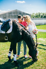 Young couple stay and walking near black horse at green farm