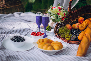Picnic Time! Fresh food on grass in the garden. Basket on blanket glasses of champagne.
