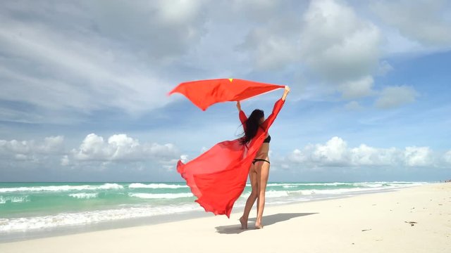 Young woman in red dress stand on caribbean coast with vietnamese flag at her arms