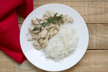 Top view of cooked chicken with white sauce and rosemary and served on wooden table with red napkin. Healthy eating concept