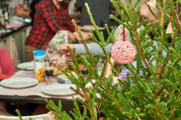Decorated Christmas tree on foreground with family at festive table on the background