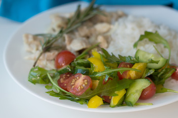 Fresh salad with cherry tomatoes, arugula leaves, cucumber and capsicum slices served with white rice and chicken slices
