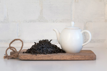 Black tea big leaves and porcelain teapot on wooden desk.