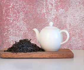 Black tea big leaves and porcelain teapot on wooden desk.
