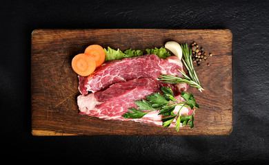 Raw marbled beef on a cutting board. On a black background.top view