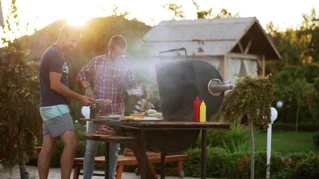 Two Caucasian males making hamburgers with fried meat and buns near barbecue grill in slowmotion
