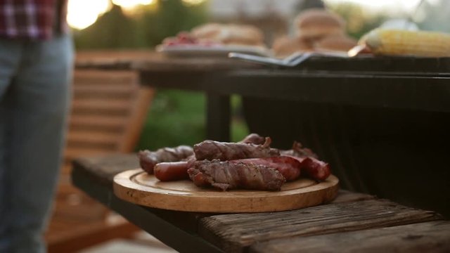 Wooden plate with fried meat adn sausages near barbecue grill. Close up footage in slowmotion