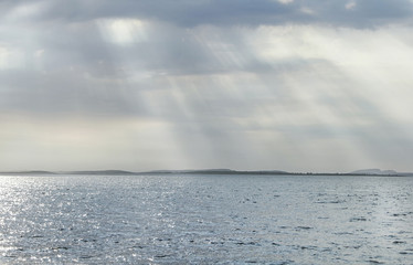 The sun's rays make their way through the clouds and the clouds over the brilliant sea and the islands of the line
