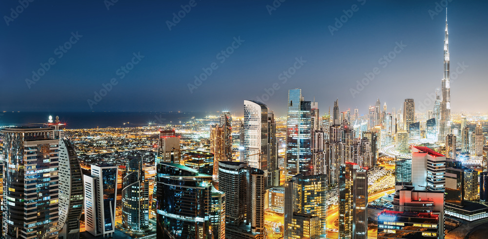 Wall mural Aerial panoramic view of a big modern city by night. Business bay, Dubai, United Arab Emirates. Colourful nighttime skyline with world's tallest skyscrapers.