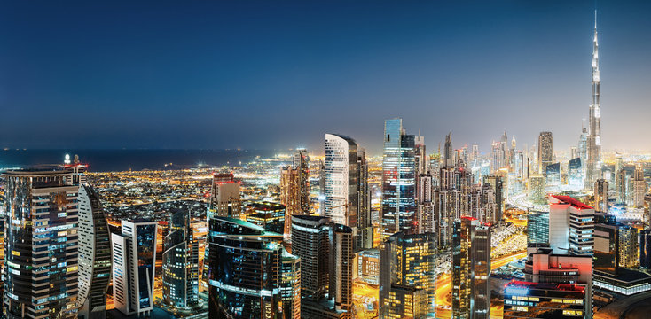 Aerial panoramic view of a big modern city by night. Business bay, Dubai, United Arab Emirates. Colourful nighttime skyline with world's tallest skyscrapers.
