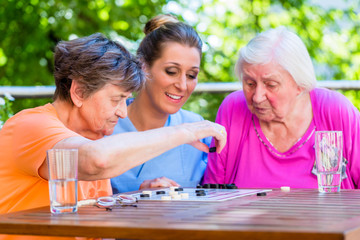 Seniorinnen spielen Brettspiel mit Altenpflegerin im Altenheim