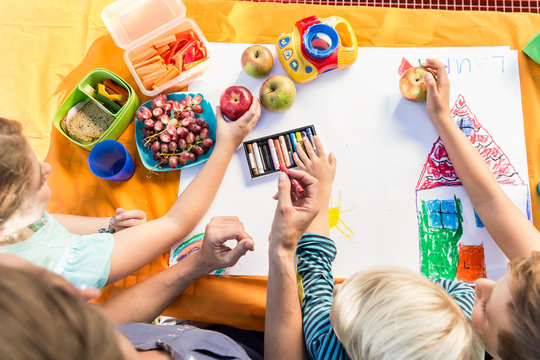 Grundschüler malen während der Frühstückspause mit Pausenbrot und Obst ein Bild 