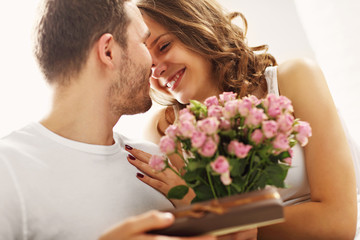 Man giving flowers and present to woman in bed