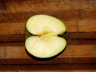 on a wooden chopping board is cut half of fresh green apple on a horizontal surface in front view