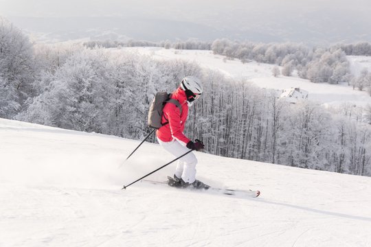 Woman skier running downhill on snow piste in mountain ski resort 