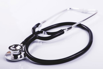 Folded metal stethoscope with black tube lying on white surface. Horizontal studio shot.