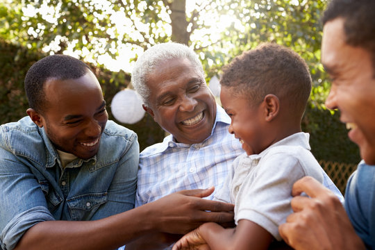 Black grandfather, sons and grandson talking in a garden