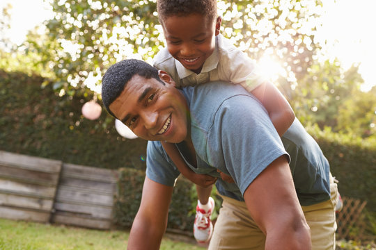 Young black boy playing on dad’s back in a garden, low angle