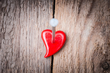 Red heart clench in wooden background with iron nail. Back focus