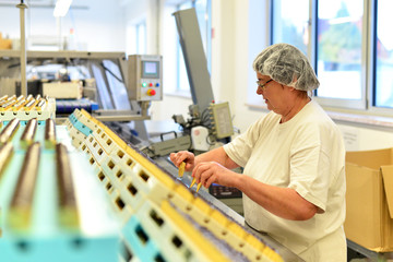 ältere Frau in einer Lebensmittelfabrik am Fliessband bei der Produktion von Süsswaren (Pralinen)...