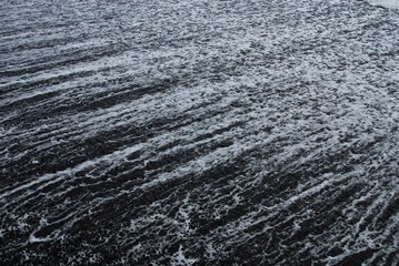 Sea foam streaking across a black sand beach as the wave retreats.  