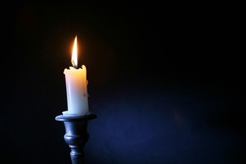 горящая свеча в подсвечнике на темном фоне