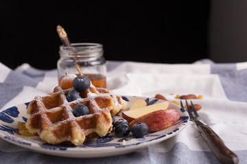 Blueberry apple waffle with honey set on a dish with a chef's hand holding spoon for a jar of honey ready to serve.