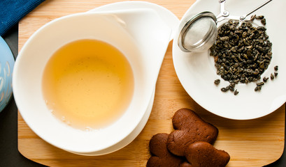 green tea leaves next to a cup of tea served with chocolate cookies